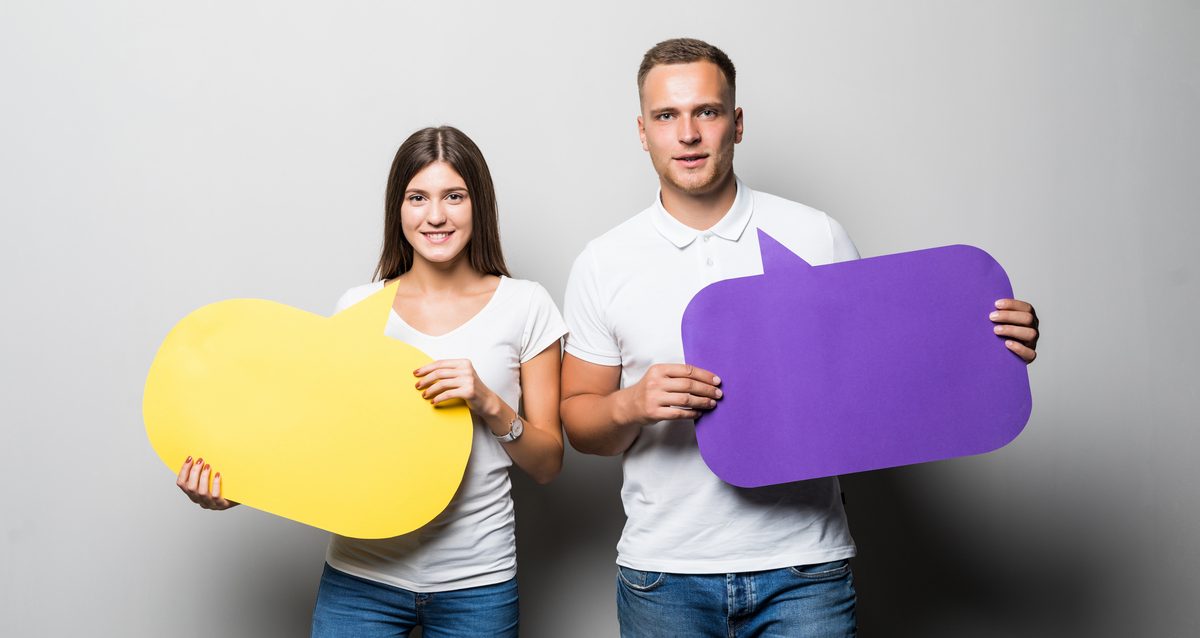 Young couple holding yellow and blue chat clouds in their hands isolated on white background