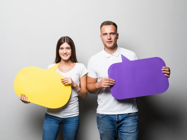 Young couple holding yellow and blue chat clouds in their hands isolated on white background