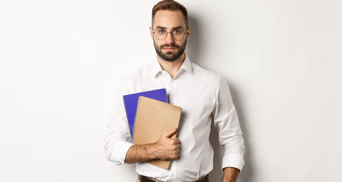 Handsome male employee holding notebooks, looking confident, standing over white background